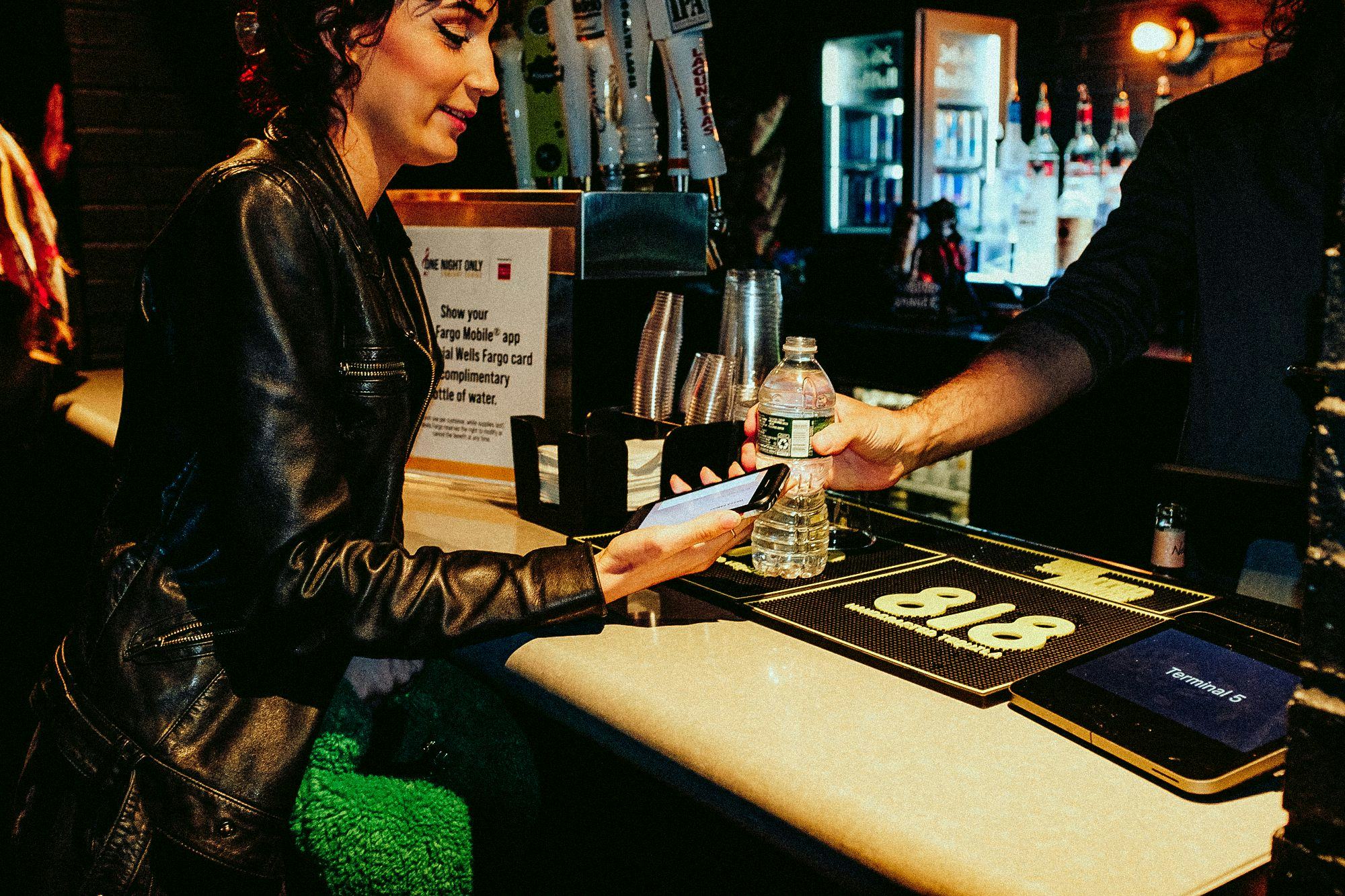 woman showing smart phone to bartender to receive a free bottle water